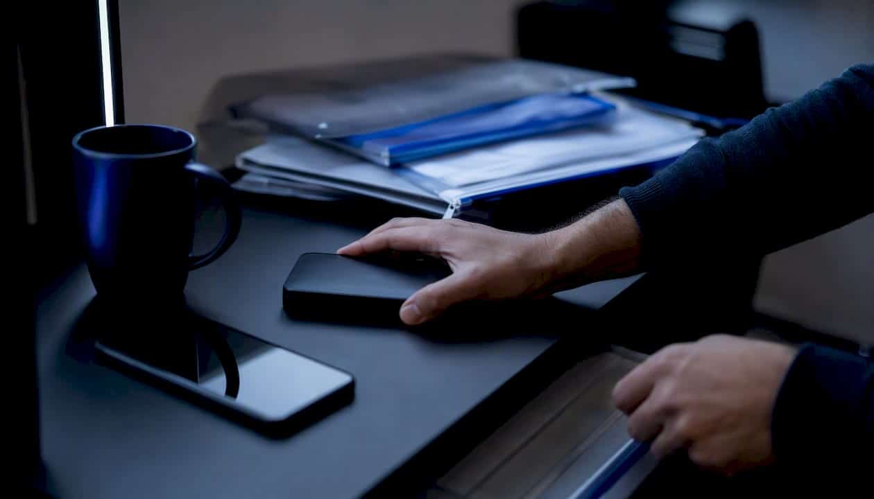 Χέρια τακτοποιούν ένα USB και ένα κινητό πάνω στο γραφείο του γραφείου.